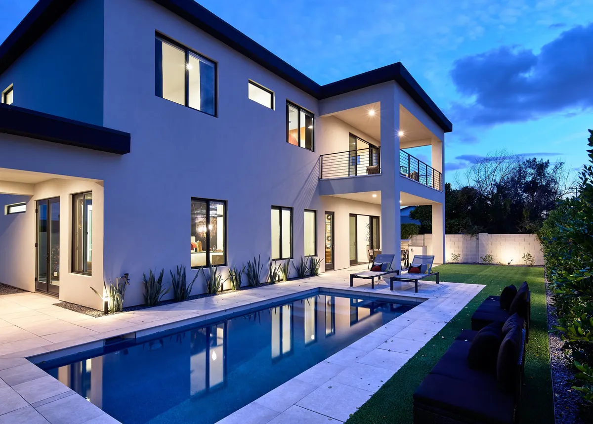 The hero image showcases a stunning modern house exterior in Scottsdale, Arizona, featuring a sparkling heated swimming pool surrounded by sleek outdoor seating, manicured landscaping, and a fire pit. The scene is set at sunset, offering tranquil desert views and a luxurious, inviting atmosphere perfect for evening relaxation or lively gatherings.