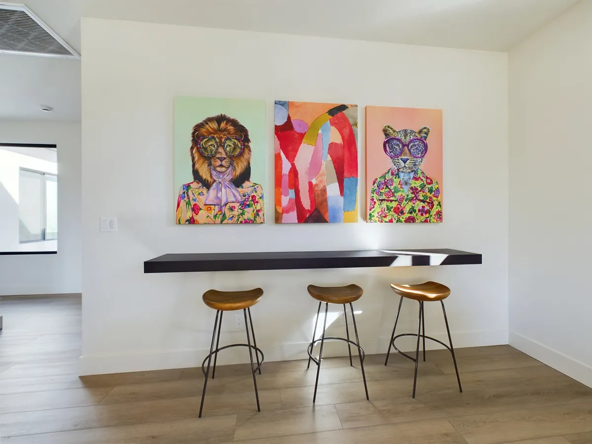 A vibrant upstairs lounge featuring colorful animal portraits, a minimalist bar table, and stylish stools. The playful decor sets a lively mood and the bar area invites casual gatherings and friendly competition.