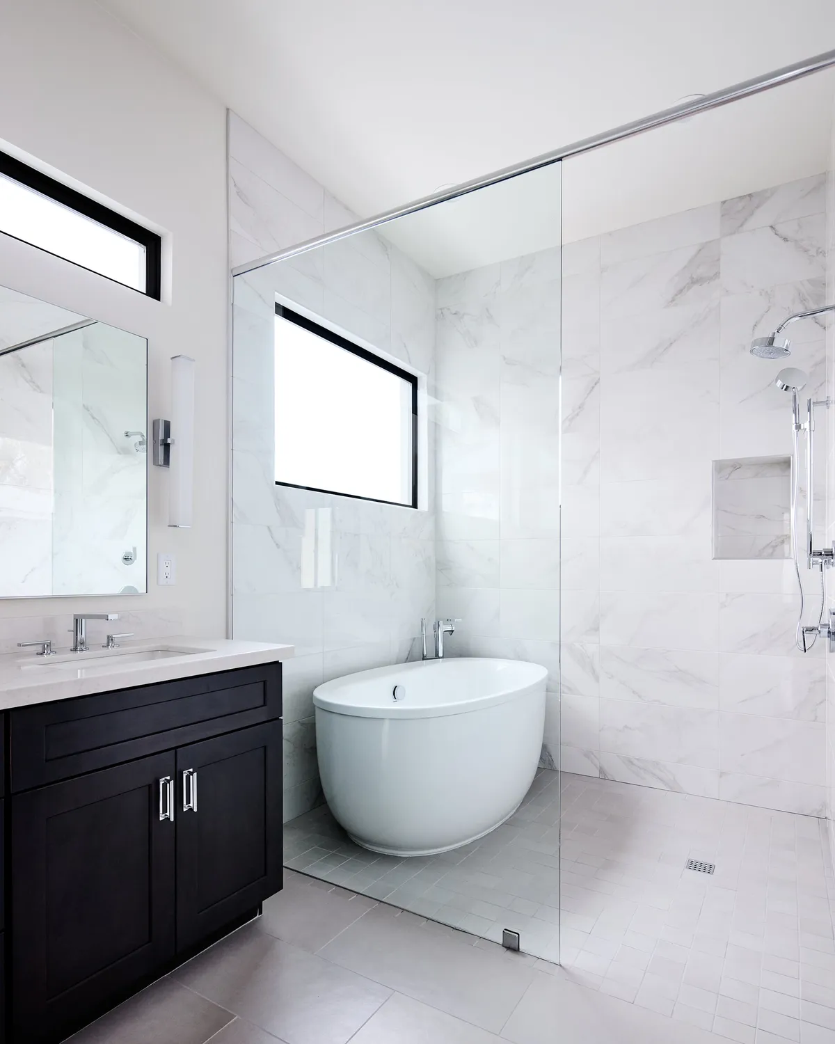 A luxurious bathroom featuring a freestanding bathtub, double sink vanity, and a large glass shower, all bathed in soft natural light. The clean lines and sophisticated finishes create a spa-like ambience perfect for relaxation and self-care.