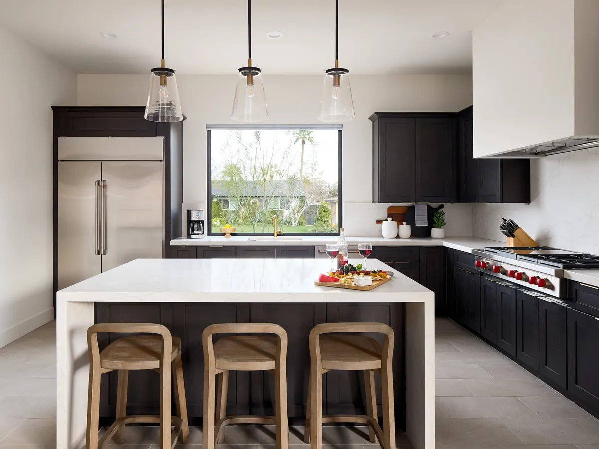 This interior shot features an inviting kitchen and dining space, with a modern island displaying an array of food, a large window overlooking greenery, sleek cabinetry, and state-of-the-art appliances. The arrangement suggests both meal prep and group gatherings.