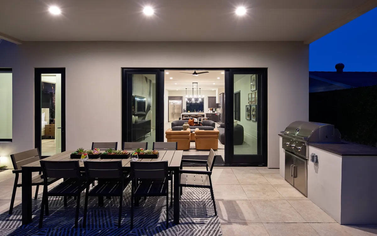 An inviting patio scene with a large dining table, an outdoor grill, and seamless indoor-outdoor flow through sliding glass doors. The setup is ideal for al fresco dining, barbecues, and gatherings under the Arizona sky.