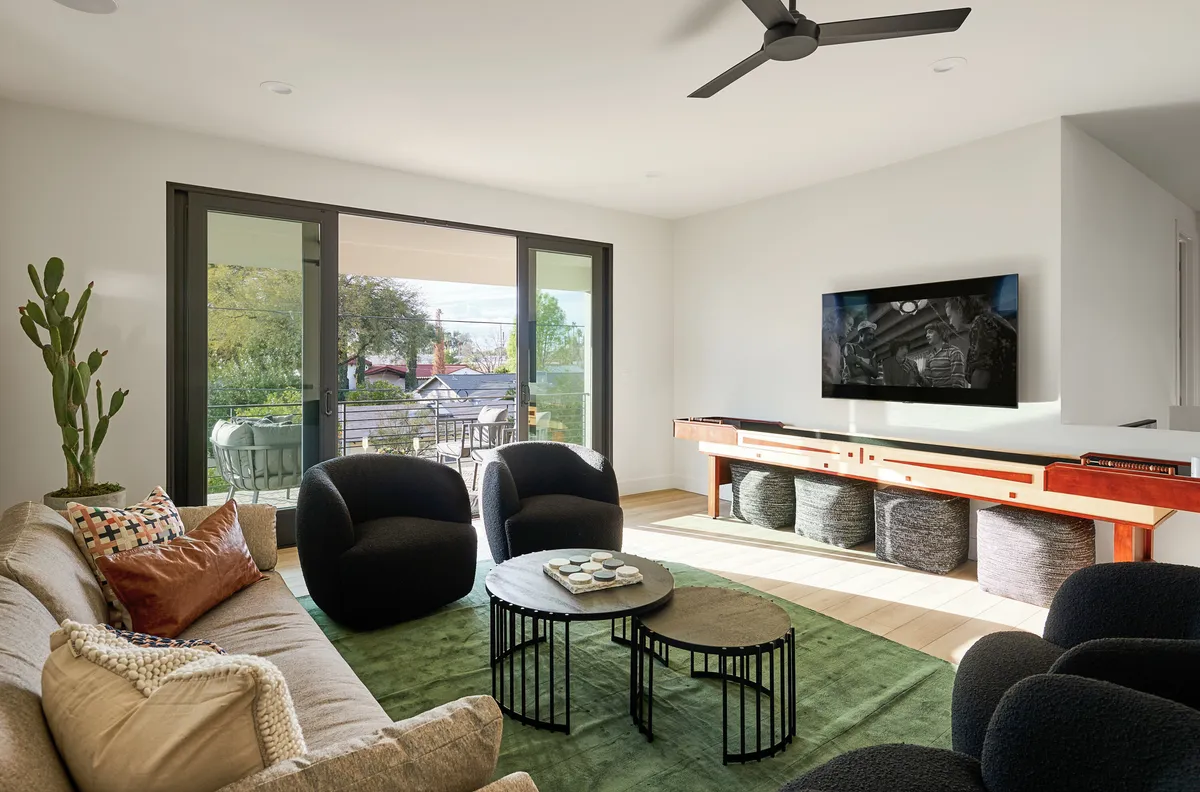 A cozy lounge setup with a comfortable sofa, black accent chairs, a coffee table, large windows, and a TV. The setting is ideal for movie nights, social gatherings, or casual relaxation, with warm light and an inviting atmosphere.